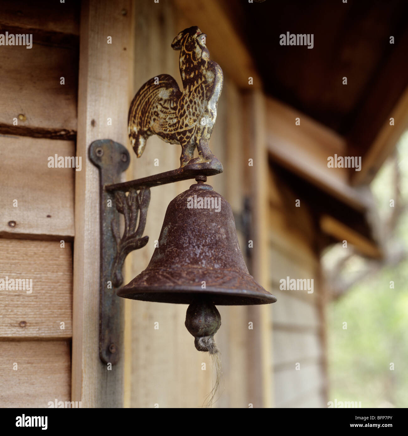 Rostige Glocke mit dekorativen Hahn an der Seite eines Holzhauses Baum Stockfoto