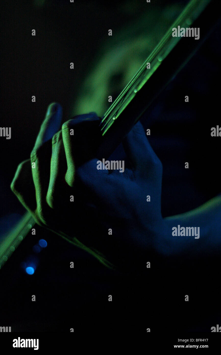 Eine elektrischer Bass-Spieler Hand wird durch grüne Bühnenbeleuchtung beleuchtet. Stockfoto
