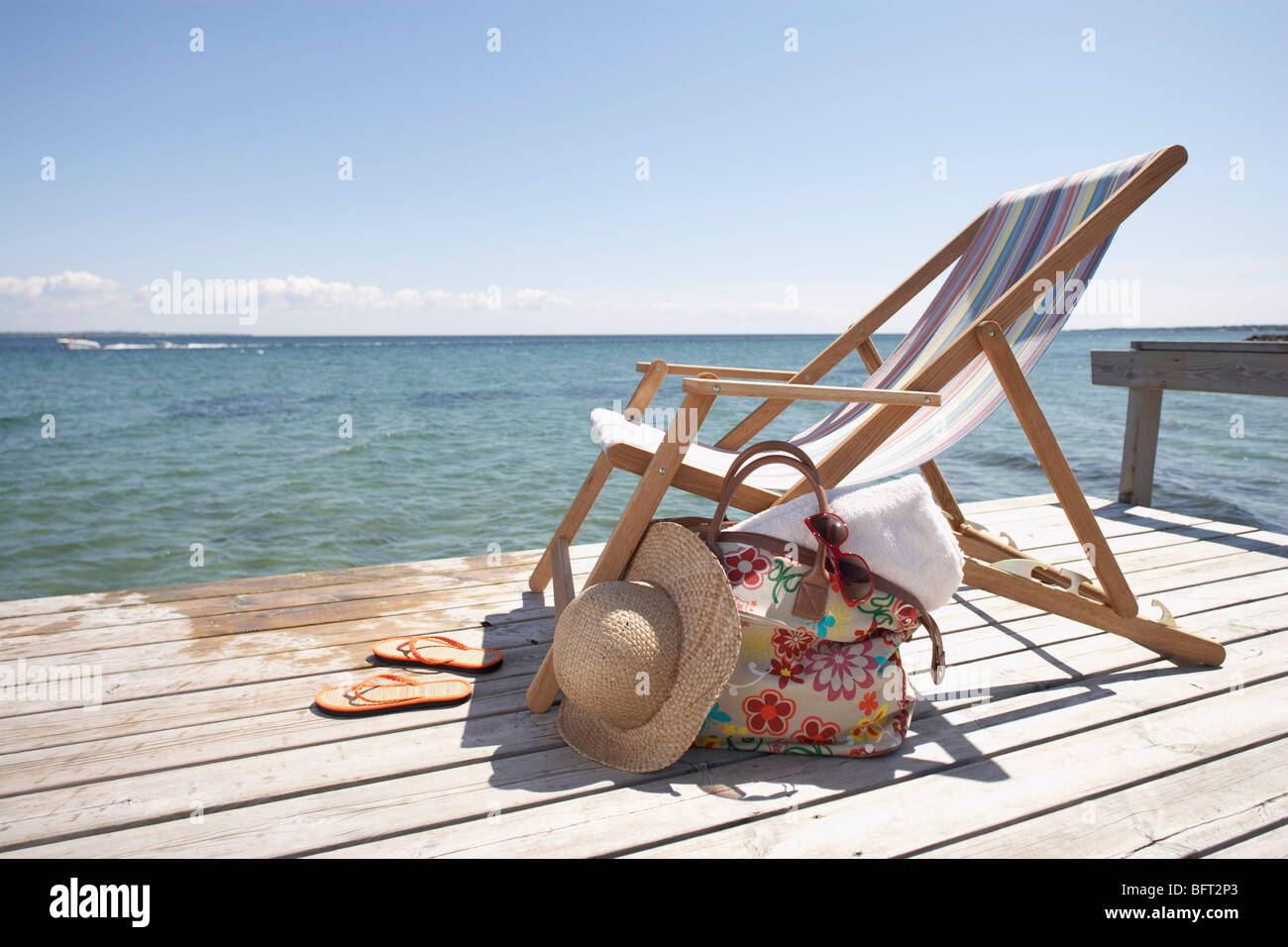 Stuhl, Hut, Flip Flops und Tasche am Dock Stockfoto