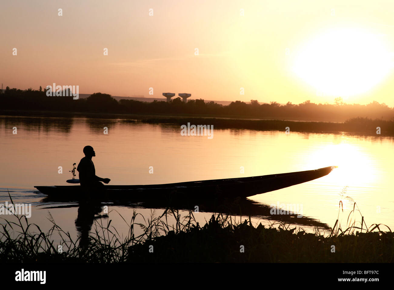 Fischer in ein kleines Boot überqueren einen Fluss bei Sonnenuntergang Stockfoto
