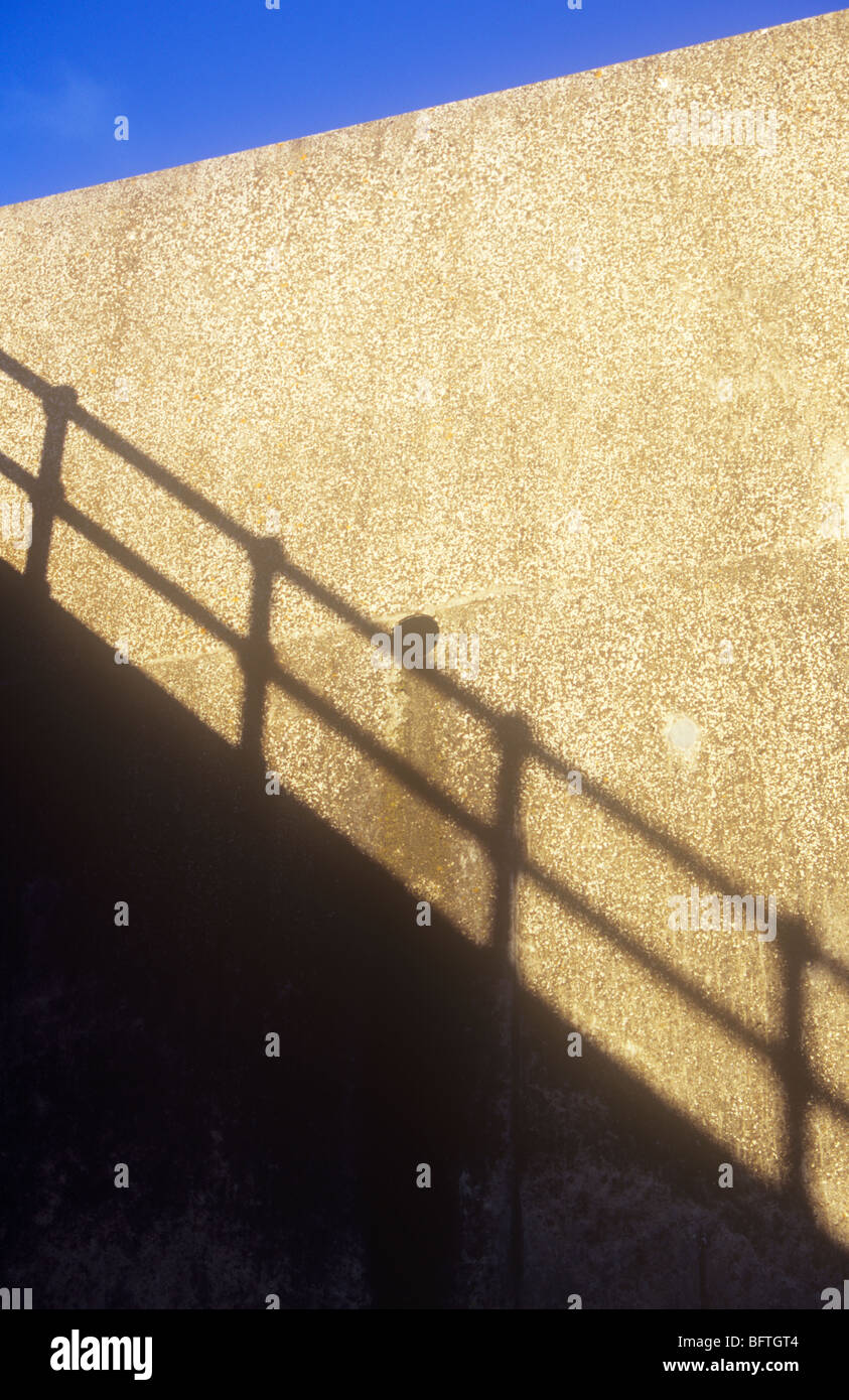 Schatten der Mauer mit Geländer auf strukturierte Creme Wand mit Entwässerungloch unter Dreieck des blauen Himmels Stockfoto