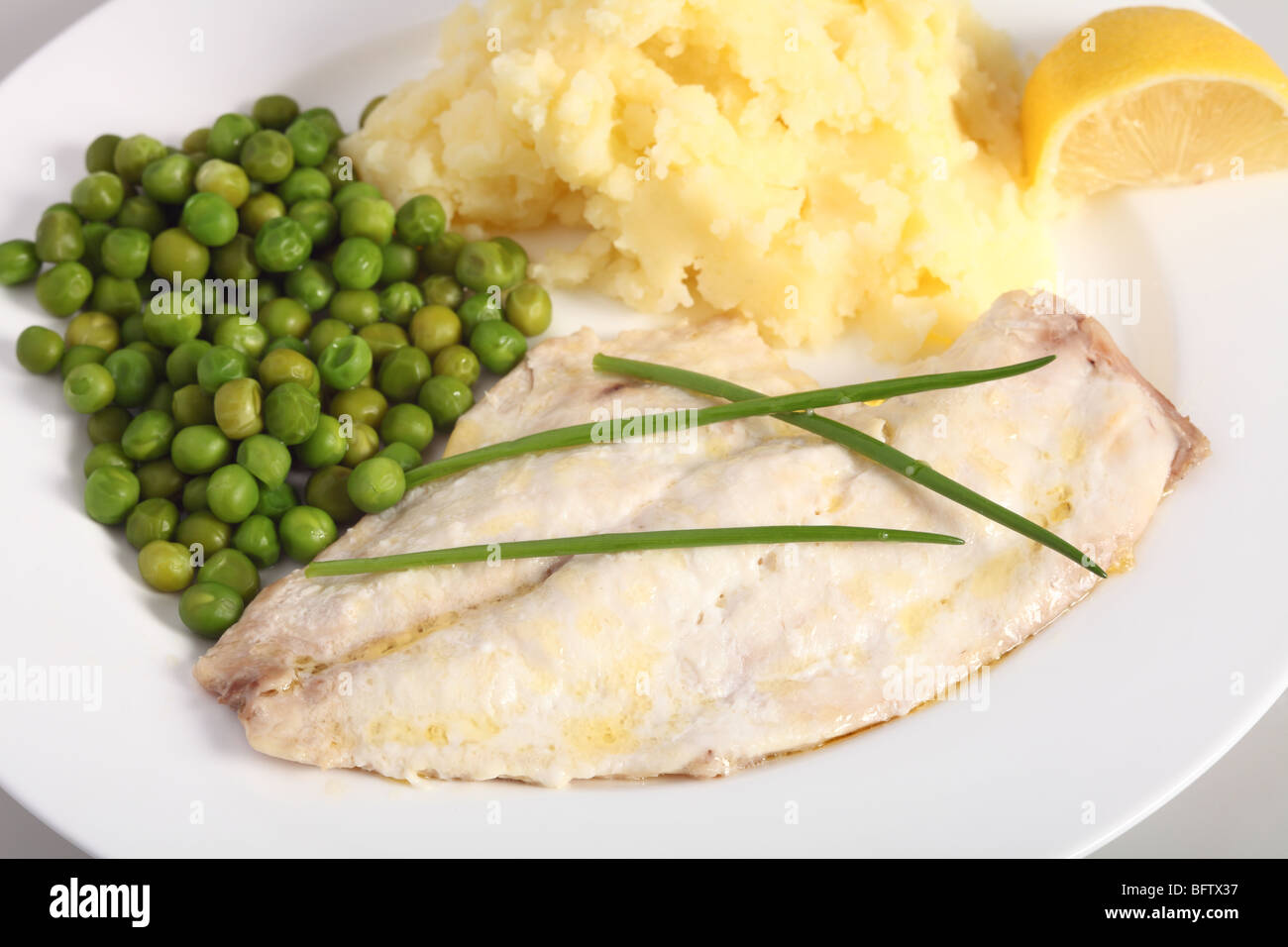 Eine gesunde Mahlzeit gebackener Fisch mit Kartoffelpüree, Erbsen gekocht und einen Keil von Zitrone Stockfoto
