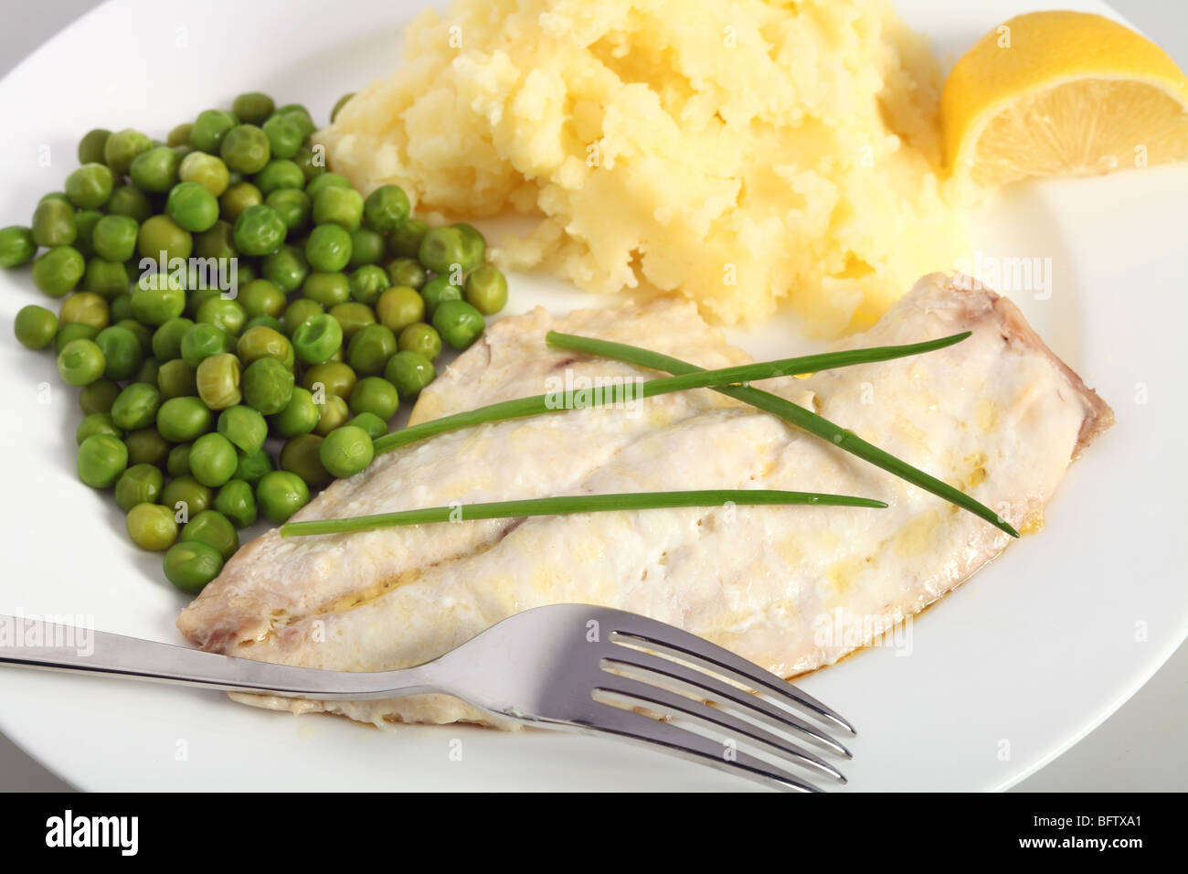 Gebackene Fischfilets serviert mit gekochten Erbsen und Kartoffelpüree und garniert mit Schnittlauch. Stockfoto