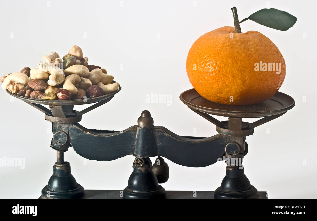 Balance-Waage mit einem orangefarbenen einerseits und einem Haufen Nussmischung auf der anderen Stockfoto