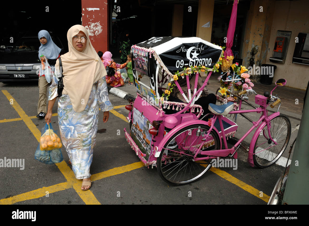 Malaiische oder malaysische muslimische Frau beim Einkaufen, vorbei am farbenfrohen Pink Tricycle oder Tricycle Rickshaw, Kuala Terengganu, Malaysia Stockfoto