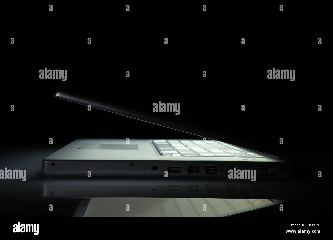Laptop Notebook mit einem leuchtenden Bildschirm in der Dunkelheit mit textfreiraum Silber. Seitenansicht. Niedrige Schlüsselszene. Stockfoto