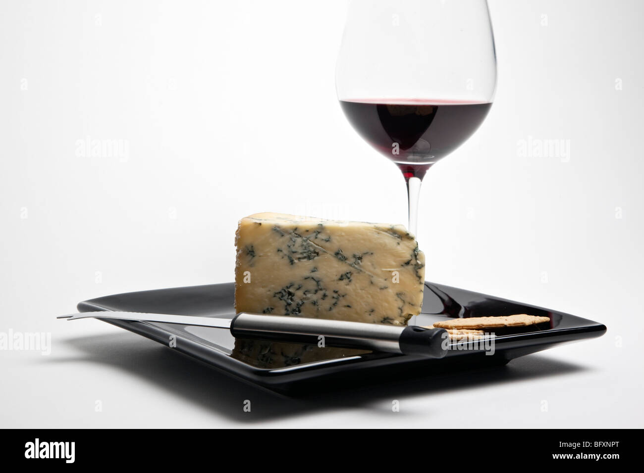 Keil von Stilton, begleitet von einem Glas Rotwein und Cracker auf einer schwarzen Platte mit Käsemesser. Stockfoto