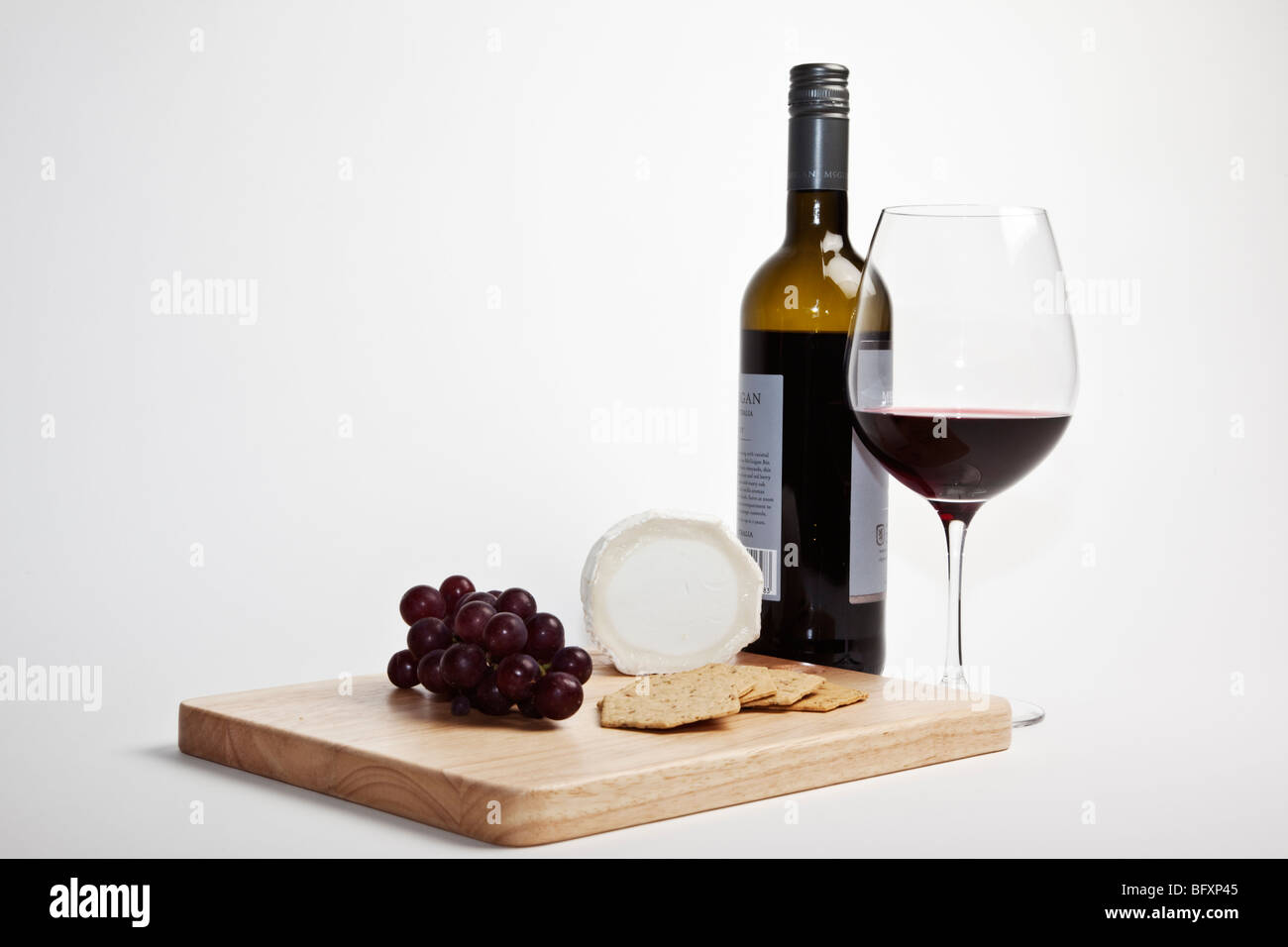 Ziegenkäse und roten Trauben mit Crackern auf eine hölzerne Käseplatte, begleitet von einer Flasche und Glas Rotwein. Stockfoto