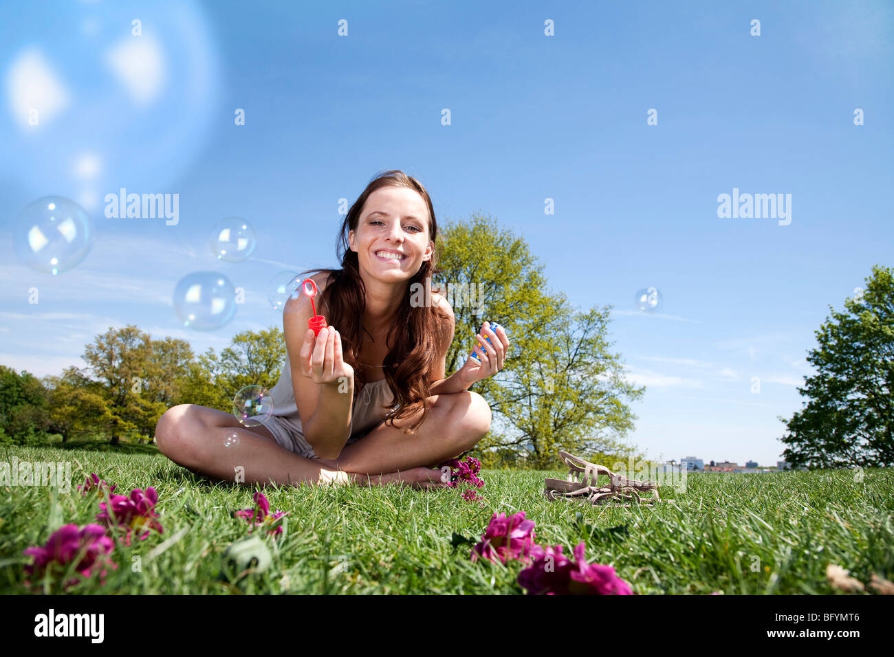 junge Frau sitzt im Rasen Seifenblasen Stockfoto