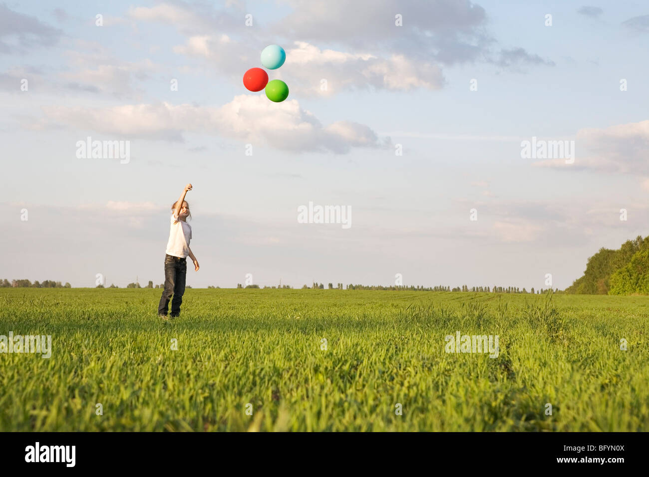 junge Mädchen stehen im Feld, die Ballons fliegen lassen Stockfoto
