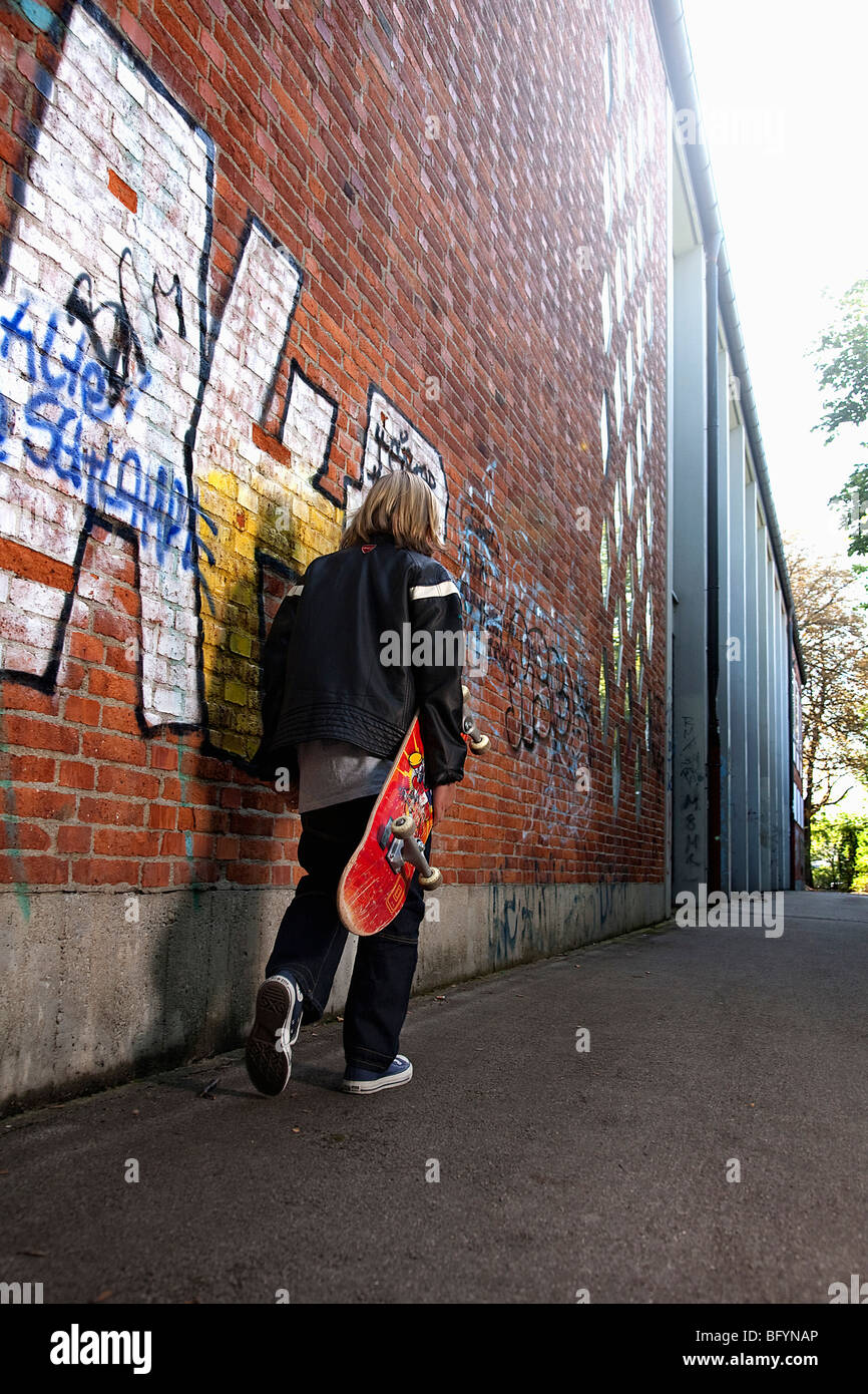 Heckansicht des kleinen Jungen zu Fuß entlang der Wand mit skatebord Stockfoto