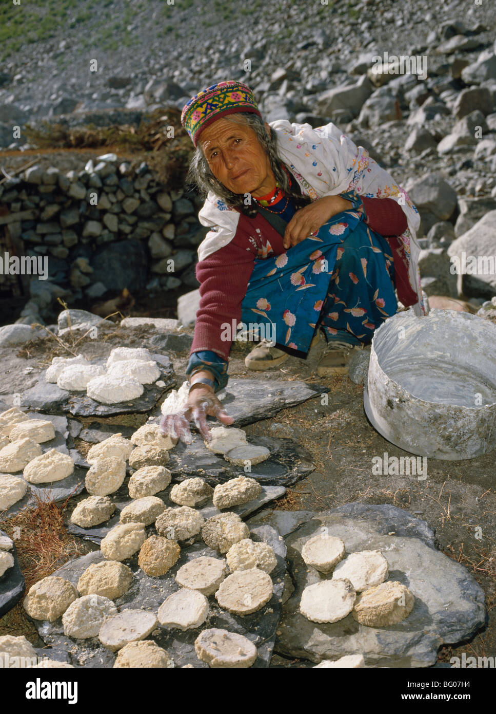 Frau in traditioneller Kleidung trocknen frisch gemacht Käse auf steinerne Tafeln, Yeshpert, Batura Valley, Nord-Pakistan, Asien Stockfoto