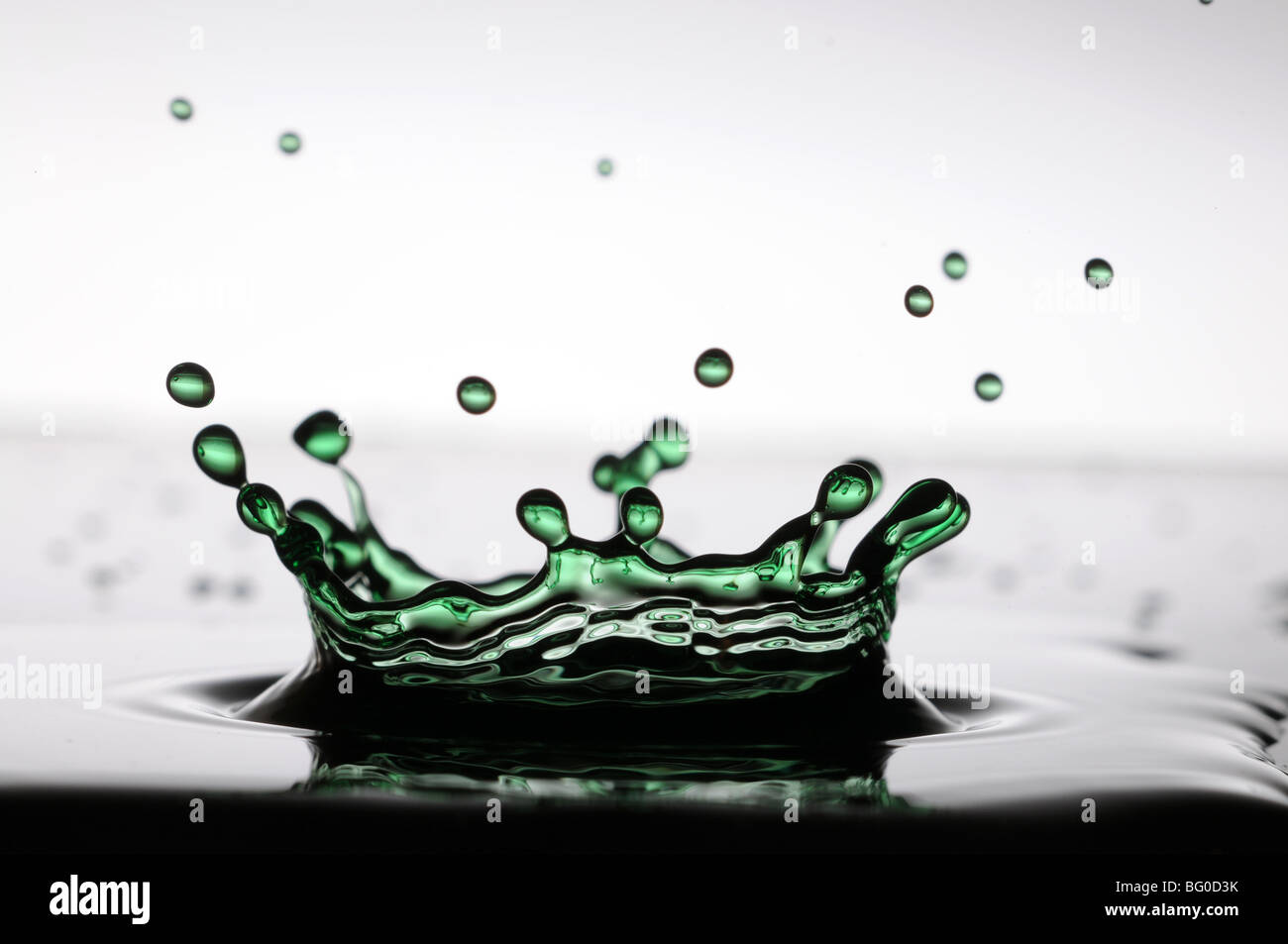 Ein Wassertropfen grüne Krönchen bilden, wie es in einer flachen Schicht Flüssigkeit spritzt Stockfoto