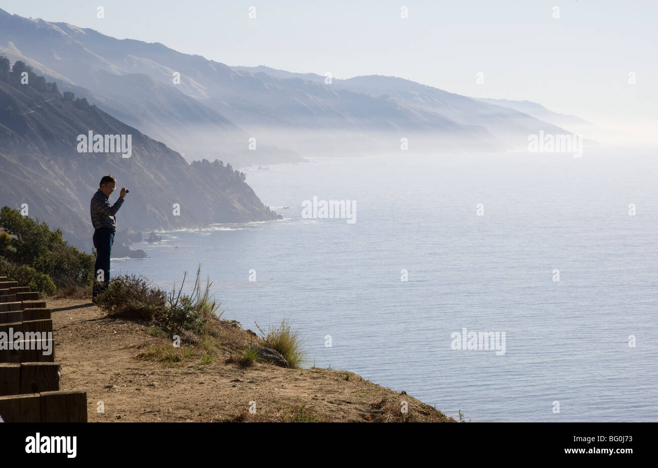 Ein Mann, der am Rande der Klippe steht und die Küste von Big Sur fotografiert Stockfoto