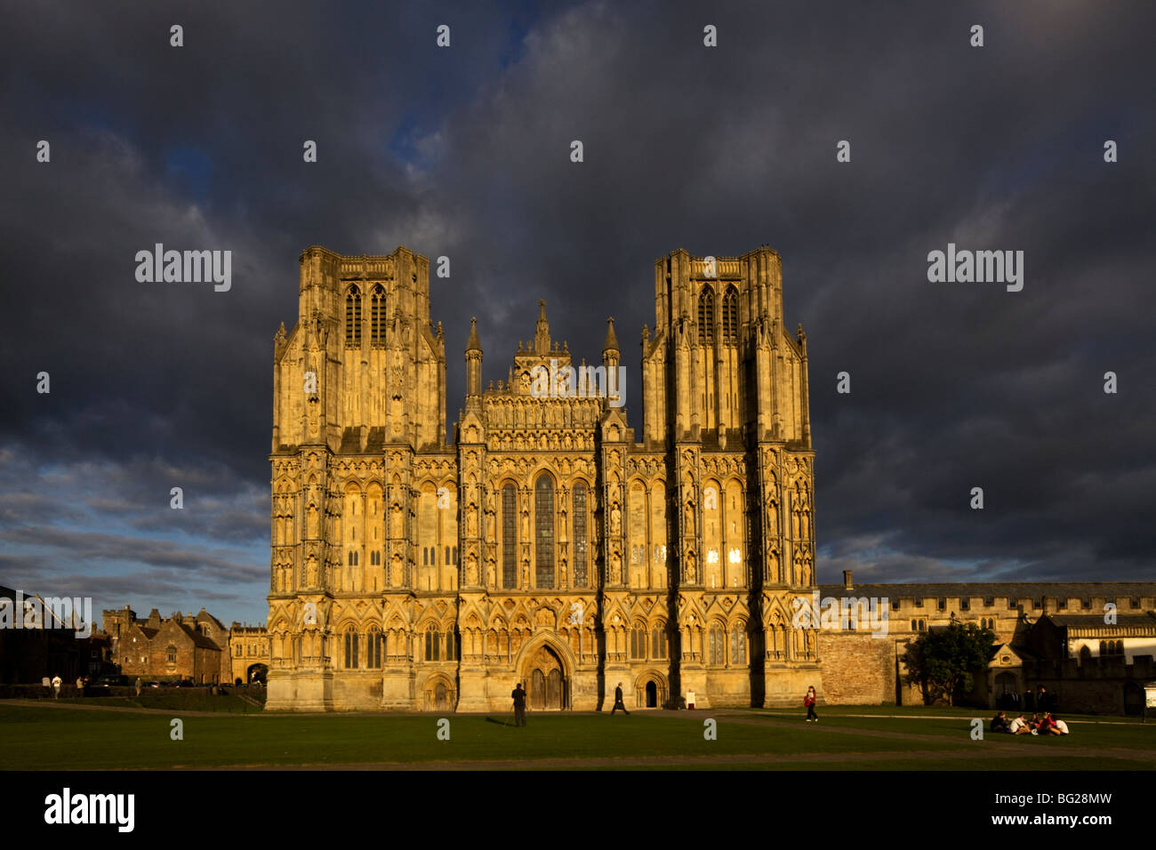 Wells Cathedral zeigt beeindruckende Westfassade mit voller Sonne und dunkle Wolken als Kulisse. Stockfoto