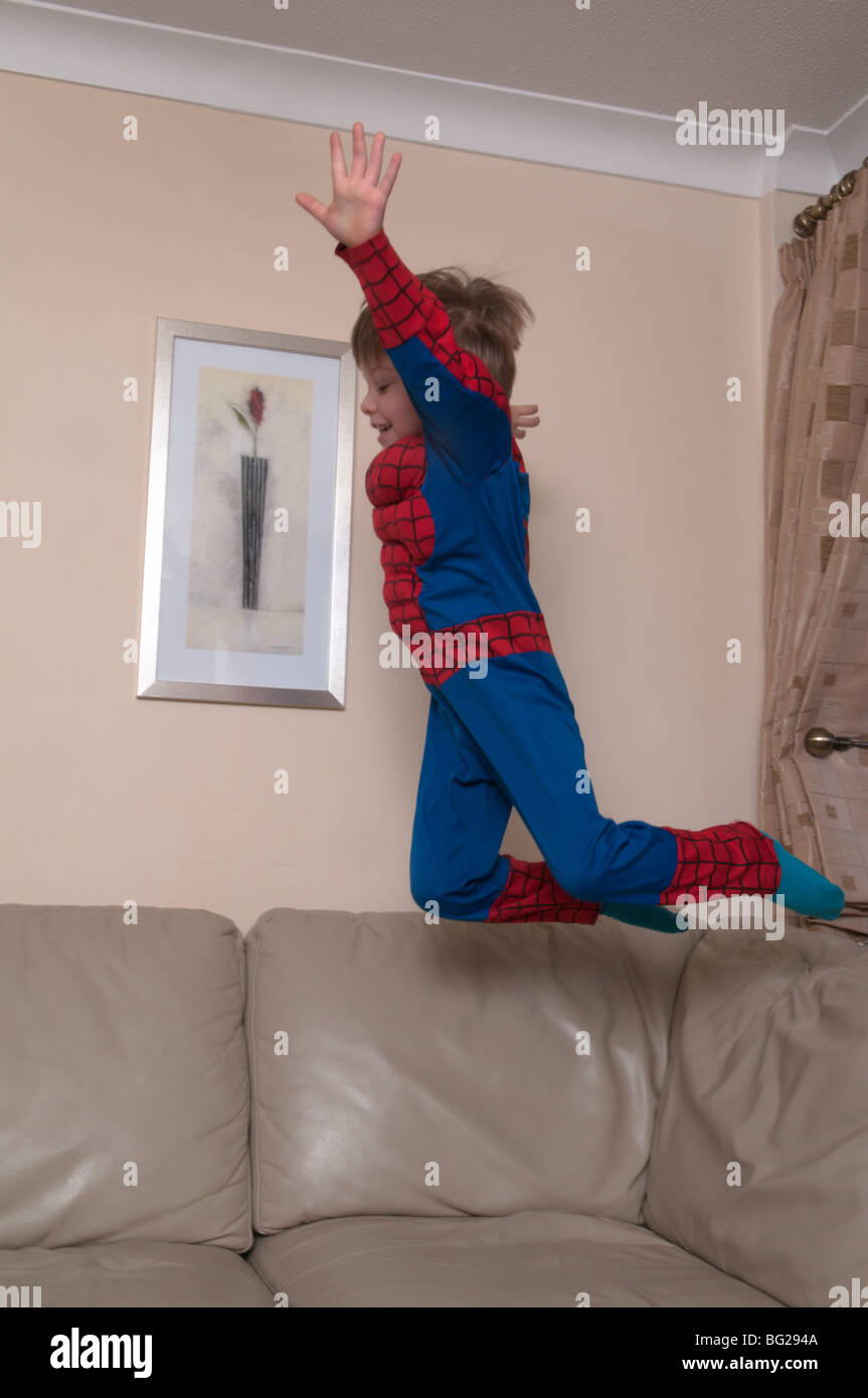 3 Jahre alter Junge in spiderman-Anzug und Maske gekleidet und auf Möbel springt. Stockfoto