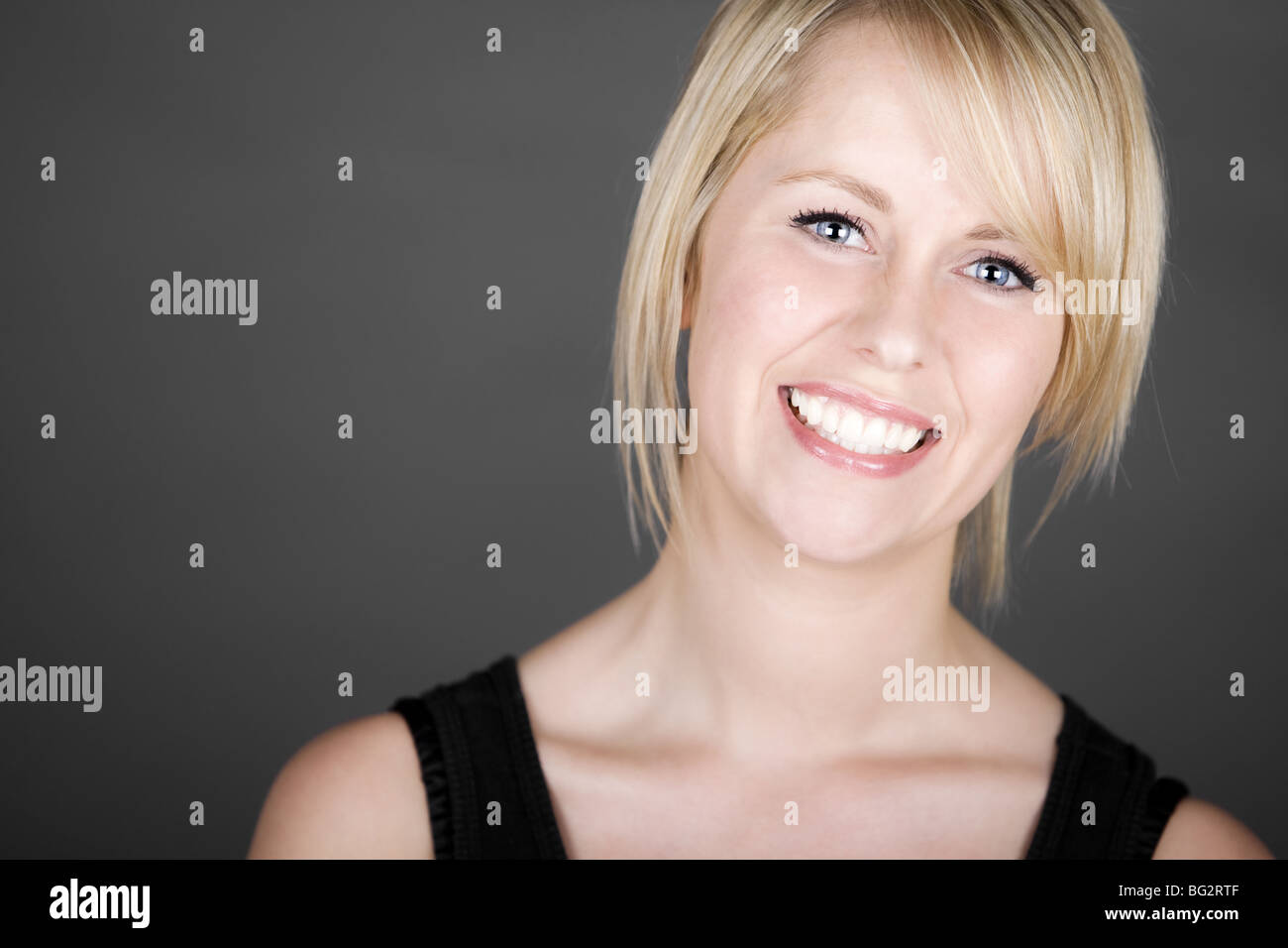 Schuss von einem schönen Lächeln auf den Lippen Blonde Mädchen vor grauem Hintergrund Stockfoto