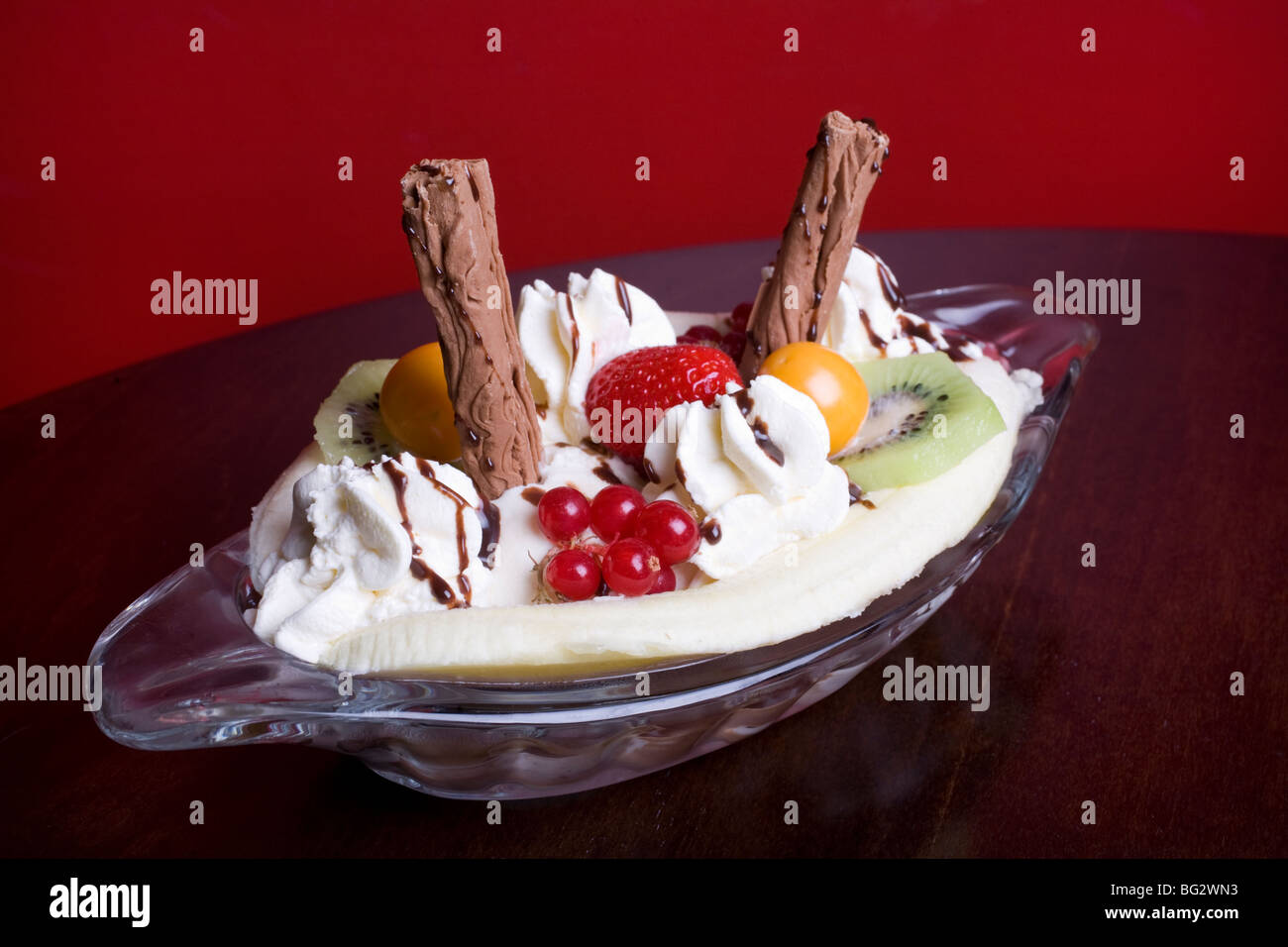 Banana Split mit Kiwis, Erdbeeren, Johannisbeeren, Physalis, Schokolade Flocken, Sahne und Schokoladensauce in einer Petrischale. Stockfoto