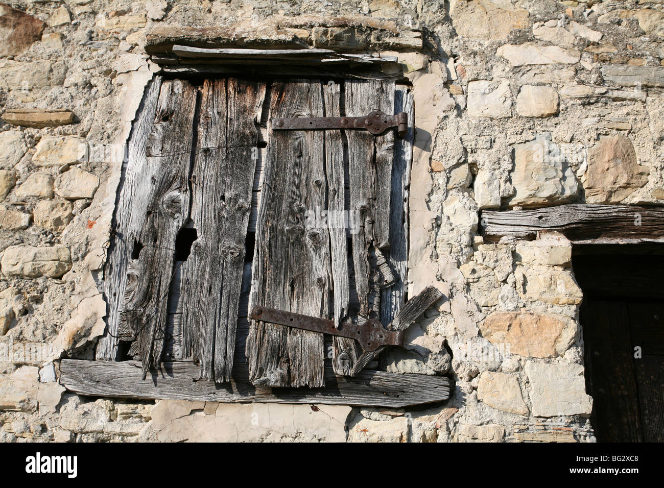 Sehr altes und verwittertes hölzernes Fensterläden, rustikales altes Steinhaus, in voller Sonne. Stockfoto