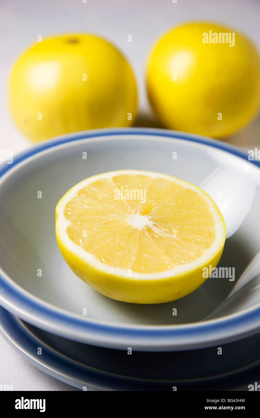 Eine halbe Grapefruit in einer blauen Schüssel und ganze Grapefruits auf einer weißen Tischdecke Stockfoto