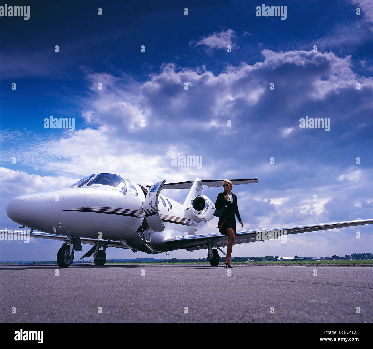Weibliche Führungskraft zu Fuß entfernt von einem Executive Jet set vor einem dramatischen Himmel Stockfoto