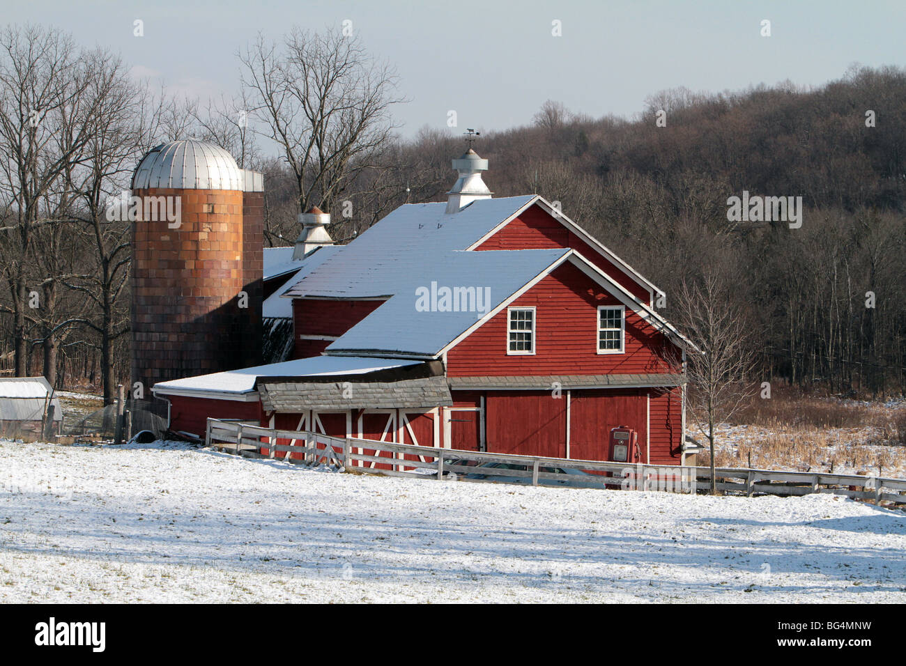Eine rote Bauernhof Scheune mit einem Silo erschossen an einem Wintertag. Schnee hat die Feld und das Dach der Scheune bedeckt. Stockfoto