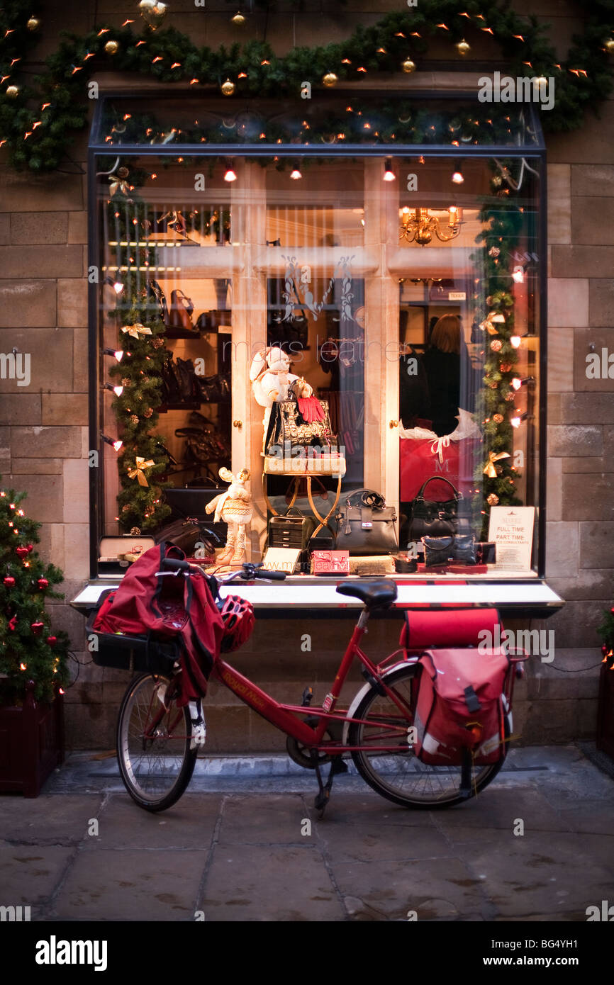 Ein Mitarbeiter der britischen Post Fahrrad vor einem Schaufenster dekoriert für Weihnachten in Cambridge, England Stockfoto