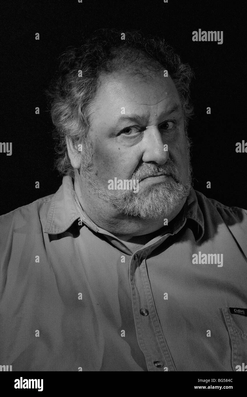 Schwarz-weiß-Porträt eines älteren Mannes mit ernstzunehmendem Ausdruck vor dunklem Hintergrund. Stockfoto