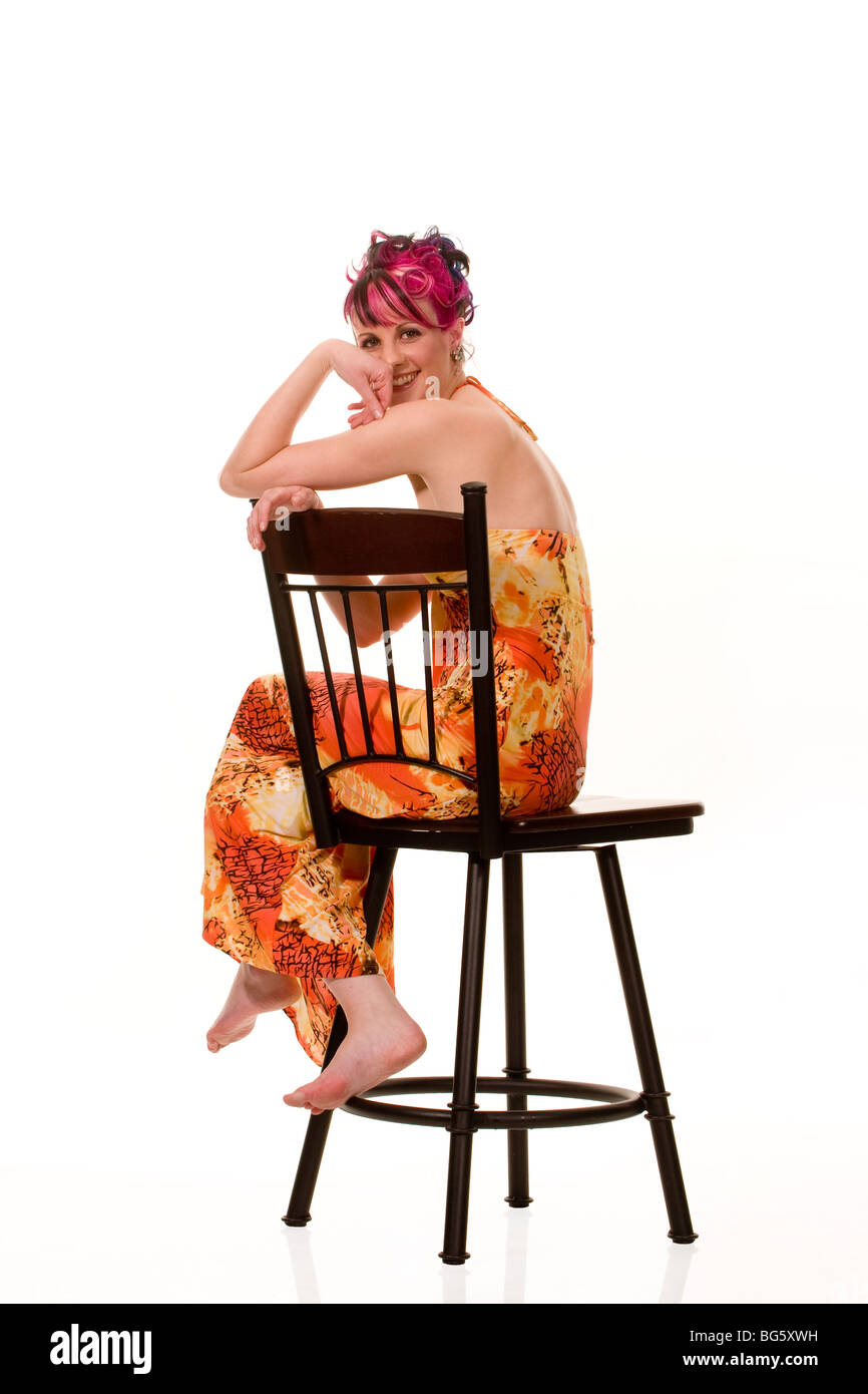 Eine junge Frau auf einem Stuhl sitzend und über ihre Schulter in die Kamera schauen. Stockfoto