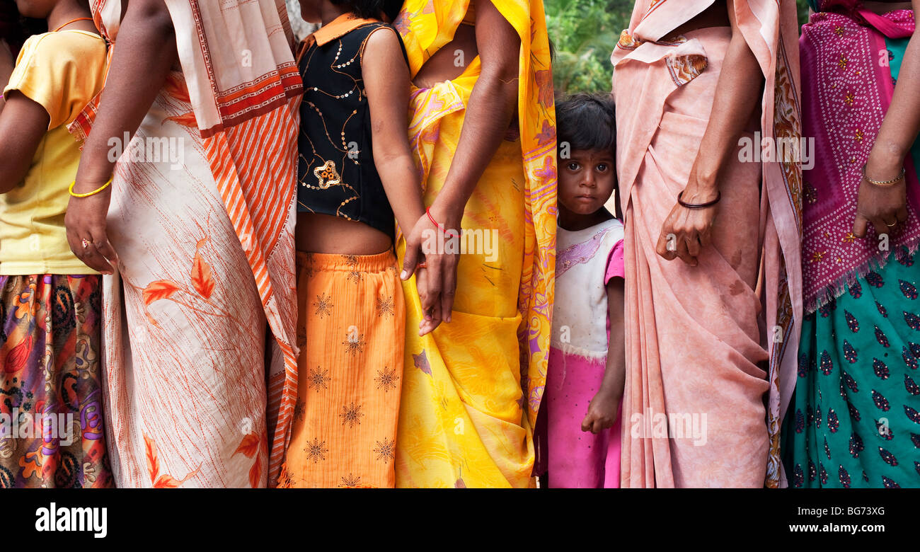 Starrte indische Mädchen stehen in zwischen Müttern tragen bunte Sari's in einer Warteschlange. Andhra Pradesh, Indien Stockfoto