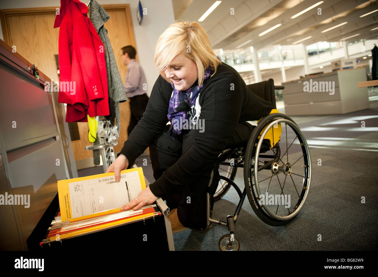 Junge behinderte Frau in einem Rollstuhl Einreichung Arbeitsunterlagen in einem modernen Büro, Uk Stockfoto