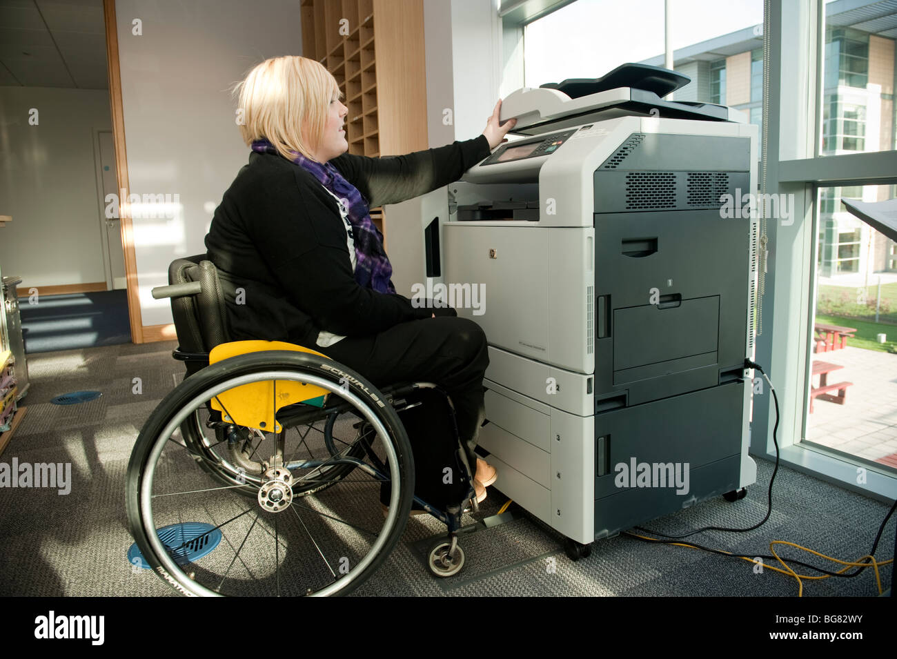 Eine junge behinderte Frau in einem Rollstuhl mit einem Kopierer Maschine in einem modernen Büro, UK Stockfoto