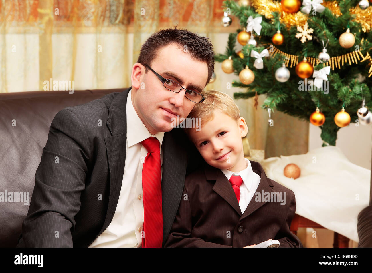 Vater umarmt Sohn neben dem Weihnachtsbaum lächelt und schaut in die Kamera Stockfoto