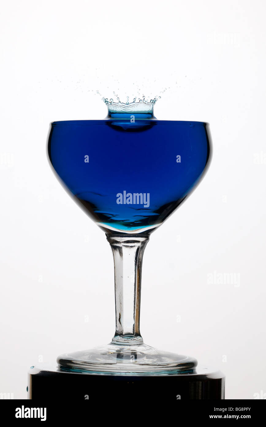 Einen blauen Tropfen Wasser in ein Glas, bilden zunächst eine Haube, dann eine Säule fallen. Stockfoto