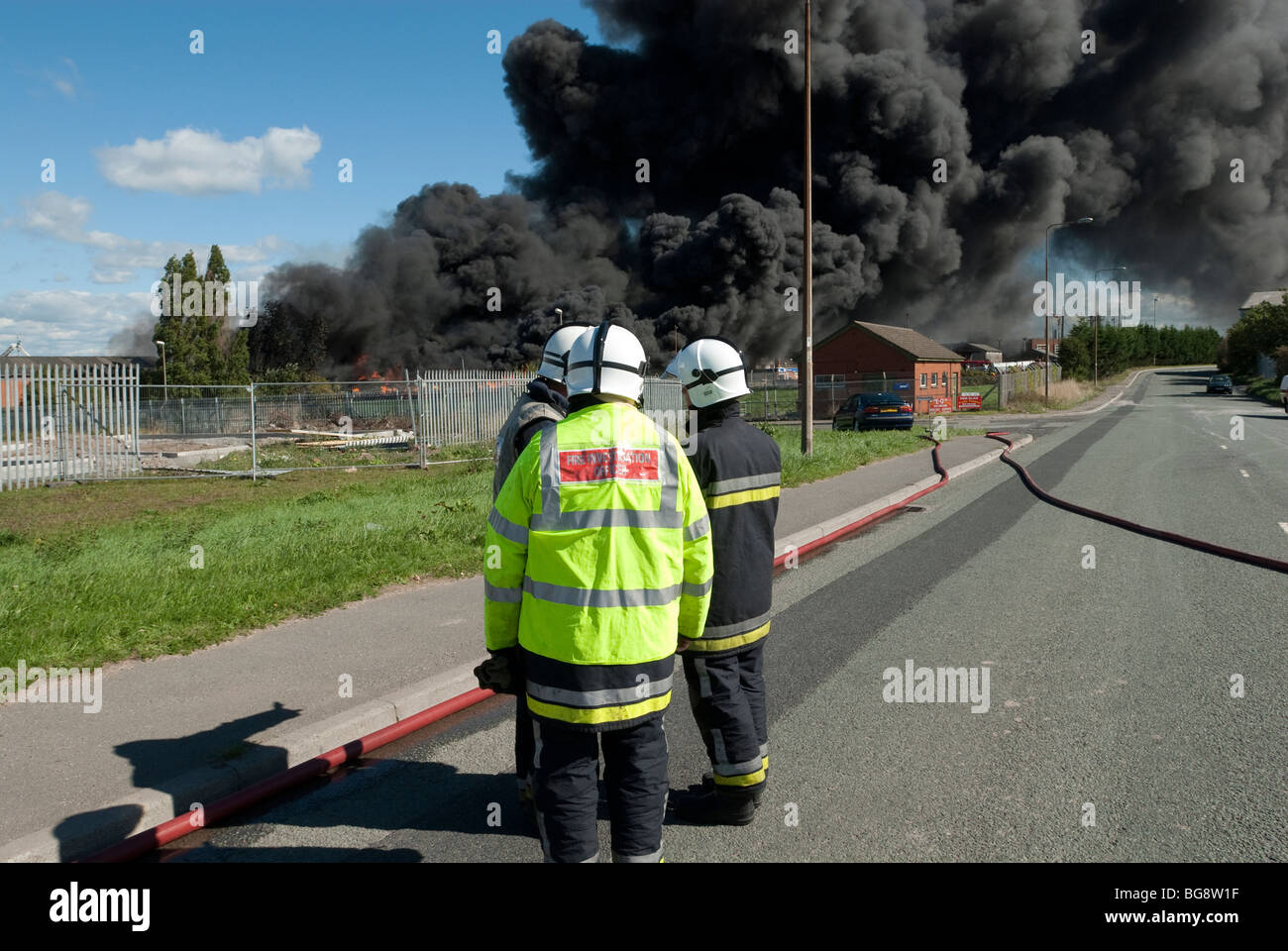 Riesige schwarze Rauchfahne gegen blauen Himmel von Fabrik-Feuer mit Feuer Offiziere Stockfoto