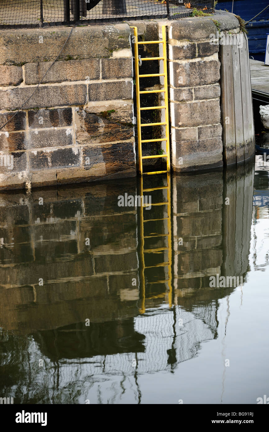 Gelbe Leiter eingebettet in eine Hafenmauer mit Reflexion Stockfoto