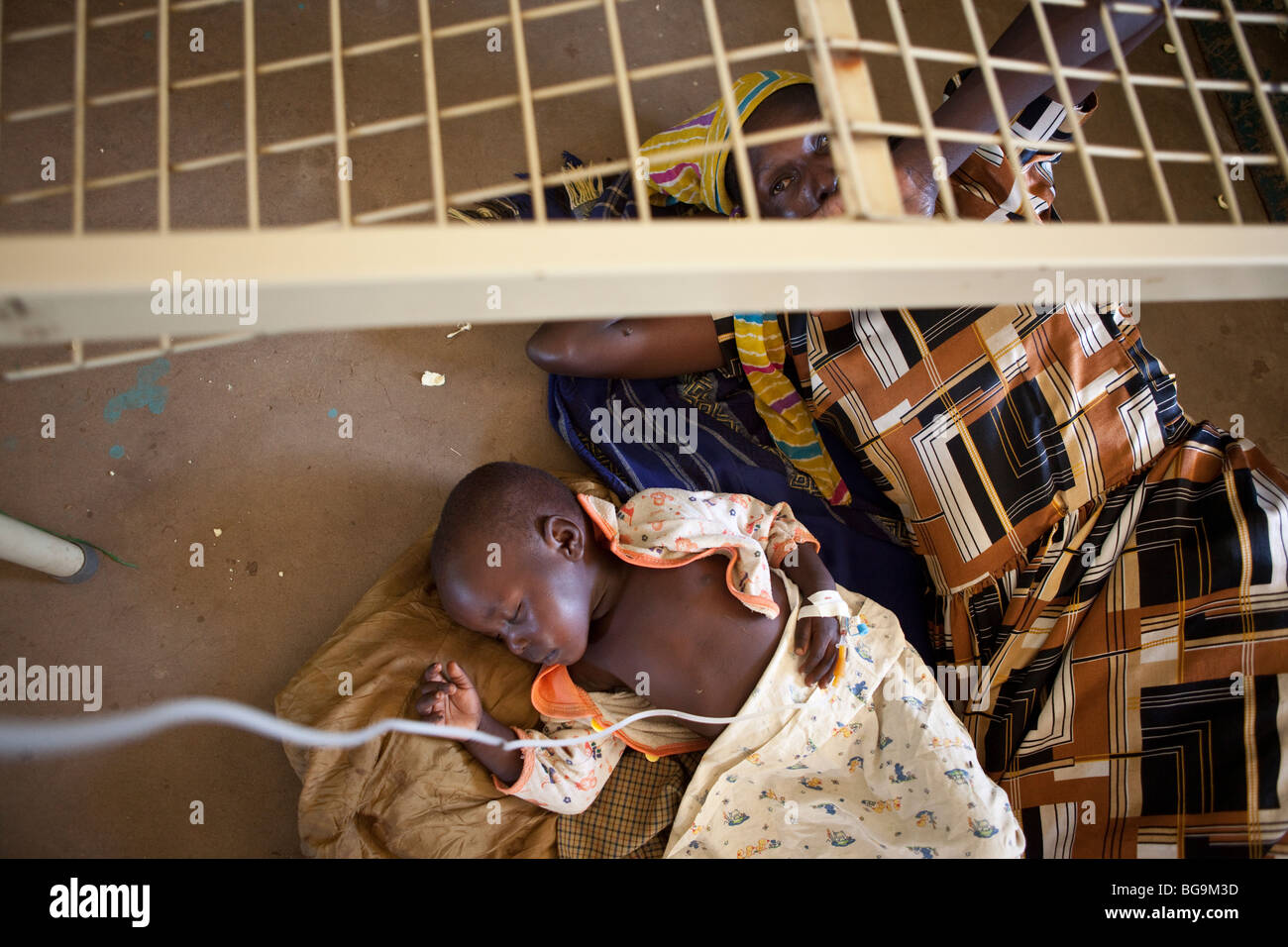Ein Kind an Malaria liegt auf dem Boden eines Krankenhauses mit seiner Mutter in Amuria, Uganda, Ostafrika Stockfoto