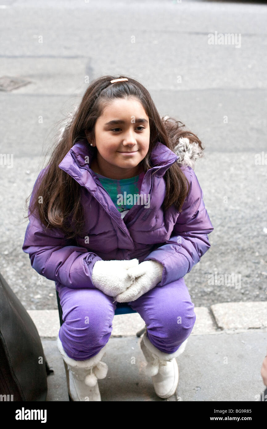 junges Mädchen mit langen, dunklen Haaren tragen lila Winter Clothingsmiles selbst bewusst für einen Bürgersteig Künstler in Midtown Manhatttan Stockfoto