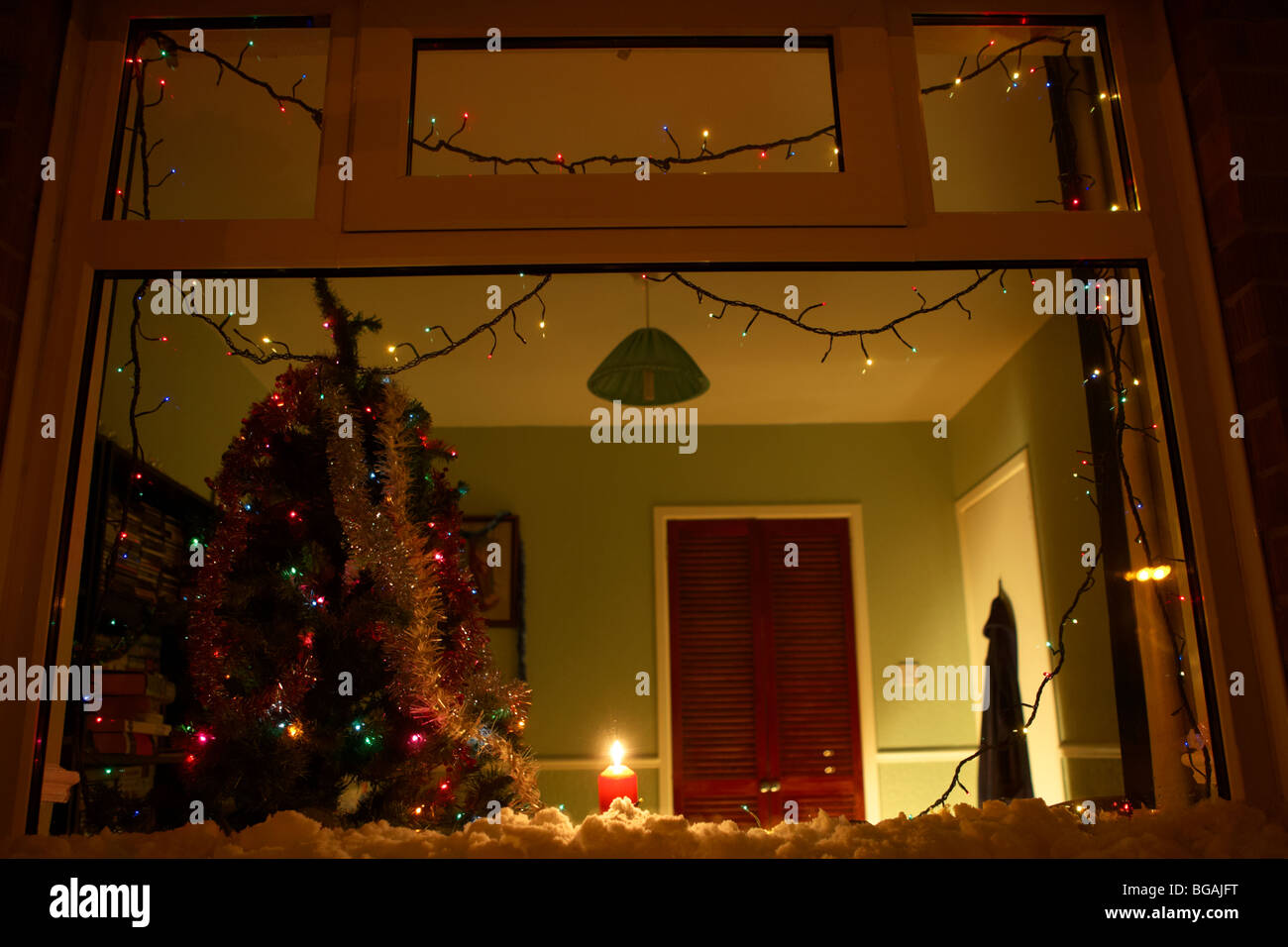 Kerze in das Fenster eines Hauses mit Weihnachtsbaum im Vereinigten Königreich mit Schnee auf der Fensterbank Stockfoto