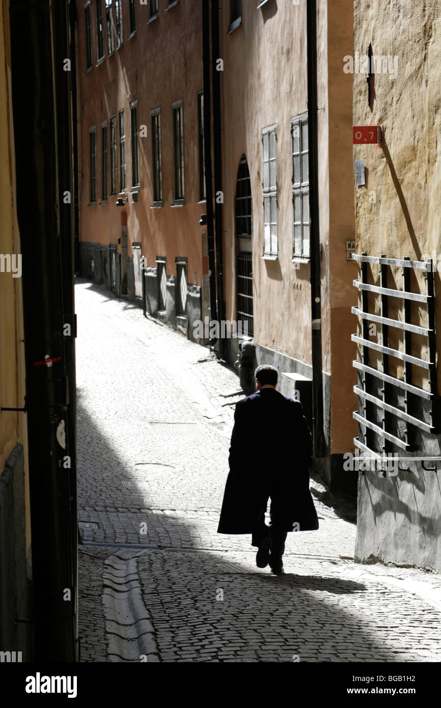 MAN IN DARK CAPE, BACKSTREET SILHOUETTE, STOCKHOLM: Ein Mann in einem dunklen cape in Silhouette geht durch die enge Kopfsteinpflasterstraße Gamla Stan Stockholm Schweden Stockfoto