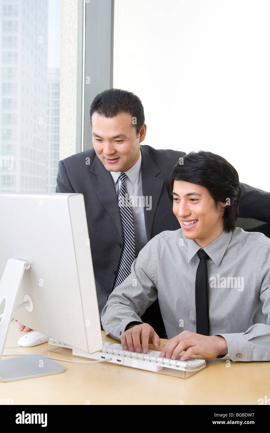 Mann im Anzug zeigt junge Mitarbeiter etwas auf einem Computer. Stockfoto