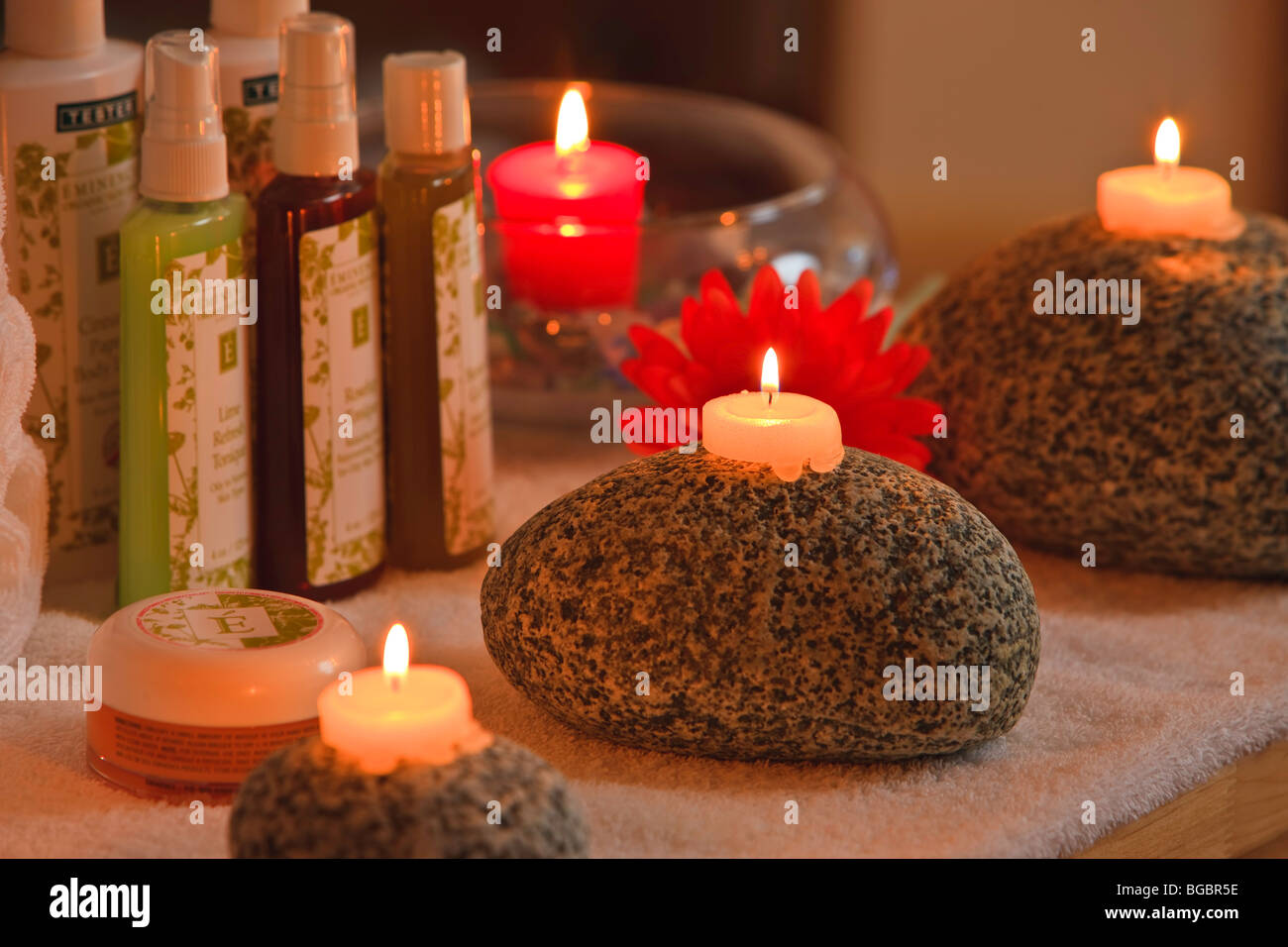 Weißes Teelicht Kerzen auf großen Westküste Felsen und eine rote Kerze in eine Glasschüssel mit Flaschen von Beauty-Produkten. Stockfoto