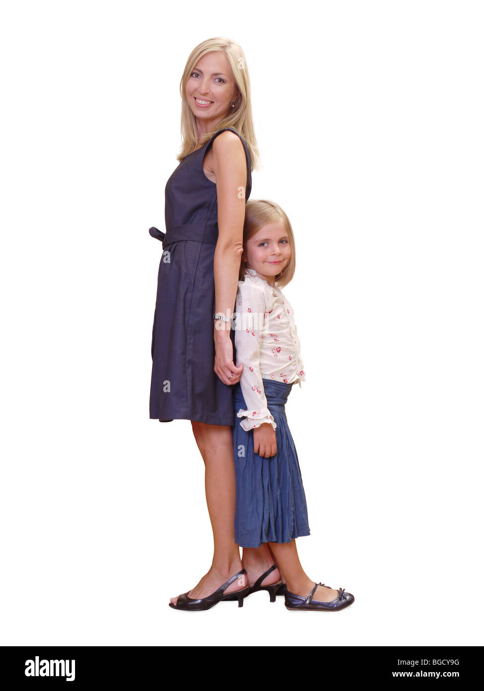 Junge Mutter und ihre süße kleine Tochter posiert stehen Rücken an Rücken auf weißem Hintergrund Stockfoto