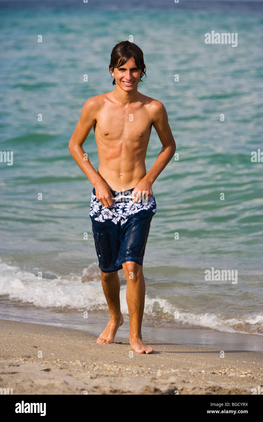 Teenager-Junge, der in Badehosen und am Strand läuft, lächelnd, Porträt. Stockfoto