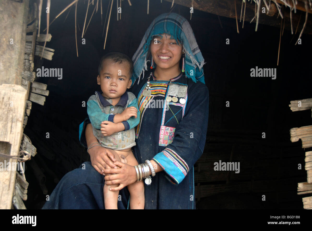 Armut, lächelnde Akha Nuqui Frau mit einem Kleinkind auf dem Schoß, gekleidet in indigo farbigen Trachten mit einem Tuch-Kopf Stockfoto