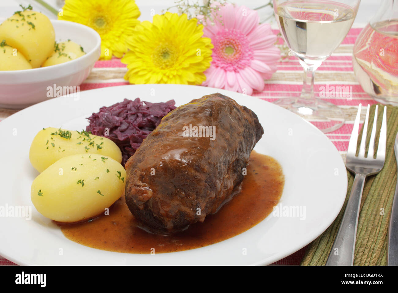 Gefüllte Rindsroulade mit Soße, Rotkohl, Salzkartoffeln und einem Glas Weißwein Stockfoto