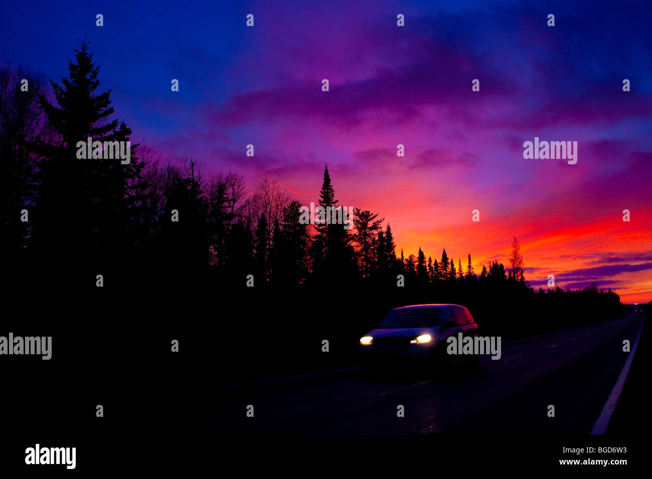 Ein Auto vergeht vor Evergreens, wenn die Sonne auf Route 117 in der Nähe von Rouyn-Norenda in Abitibi, Quebec, 21. November 2009 untergeht. Stockfoto