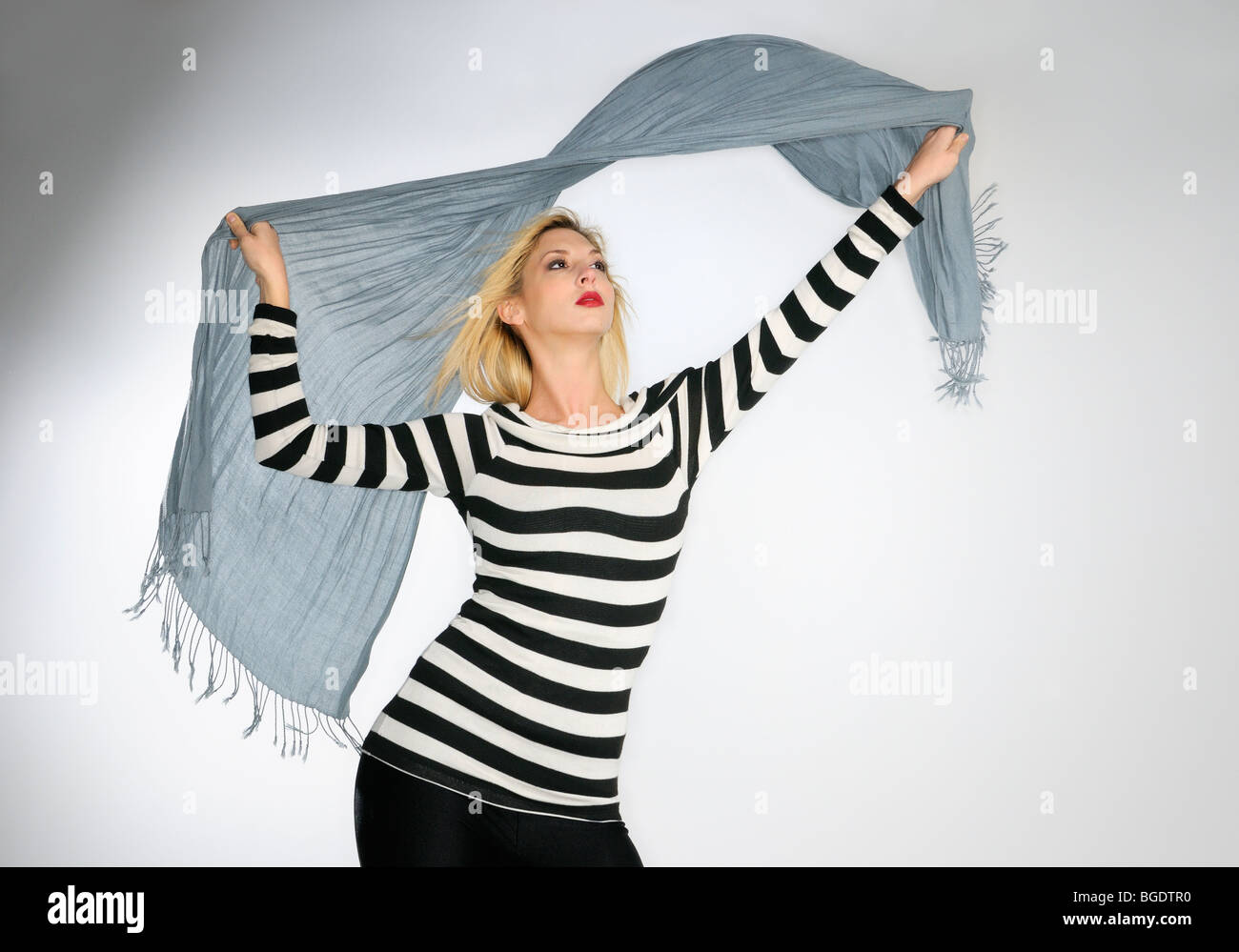Junge Frau in gestreiften Oberteil winken einen Schal in den Wind auf weißem Hintergrund Stockfoto