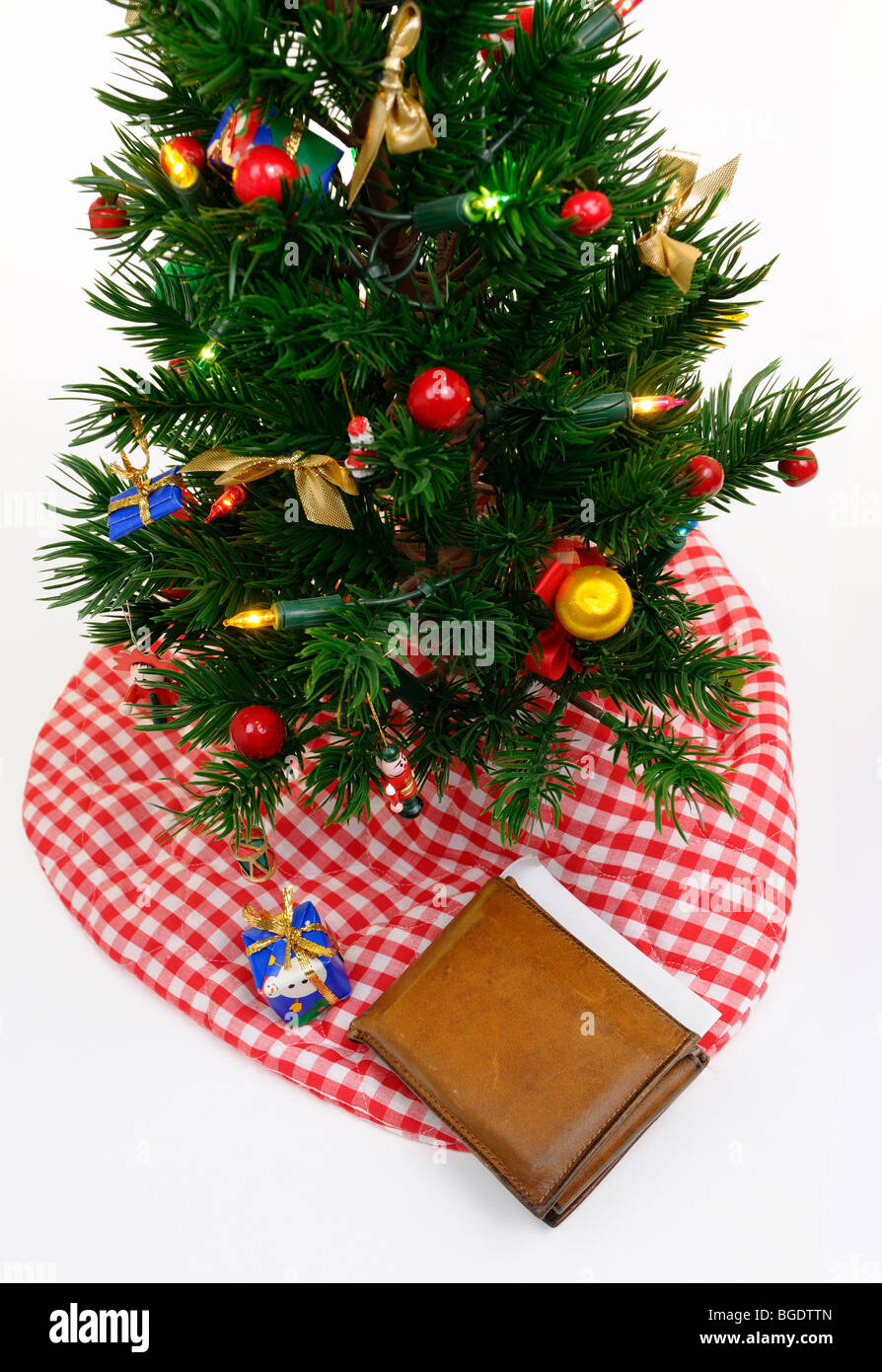 Abgenutzte alte Geldbörse mit Kreditkarten und Scheck unter dem geschmückten Weihnachtsbaum mit einem kleinen Geschenk auf weißem Hintergrund Stockfoto