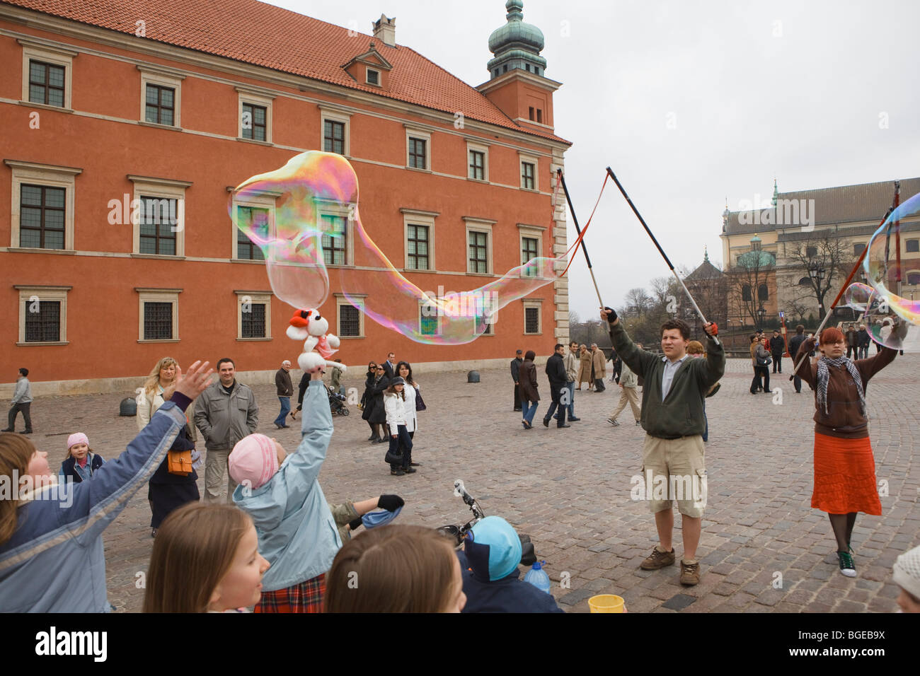 Kinder springen in Richtung einer großen Seifenblase in einen Marktplatz. Warschau, Polen. Stockfoto